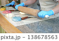 A close-up of a pastry chef rolling out soft caramel with a rolling pin in gloves on a table in a pastry shop. The production process of caramel candies. 138678563