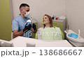 male doctor, patient attention, dental care. Dentist, man in face mask, is presenting dental model and tools to woman seated in dental chair, discussing her treatment options 138686667