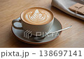 A latte with a tulip pattern in a matte white cup, framed diagonally on a wood-grain table. 138697141