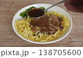 Chinese yellow egg nodles topping braised slice pork leg stew dressing black herb soup couple pickled cabbage and kale dipping spicy sour chili sauce on plate 138705600
