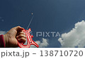Hand clamps the kite string as an unfocused kite flies in a high sky background. 138710720