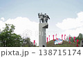 Large Soviet era concrete monument featuring two heroic figures, one with shield, another with rifle, standing together against blue sky with clouds, part of Victory Day memorial complex. 138715174