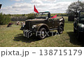 Vintage military off road utility vehicle painted army green with red flags on display outdoors under partly cloudy sky, historical war machine parked on grass for public viewing 138715179