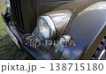 Close-up of front section of vintage military truck, showing headlight, fender, grille, and bumper, with olive green paint detail in bright daylight outdoor display 138715180