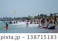 Crowded beach scene, adults and kids enjoying summer day activities, parasail flying overhead, resort buildings and palm trees lining distant shore, bright sun. Slow motion x4 138715183
