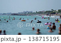 Crowd of people enjoy summer vacation swimming and relaxing in clear blue sea water, beach resort complex under bright sunny sky during daytime. Slow motion x4 138715195