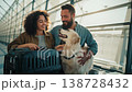A couple happily greets their golden retriever at the airport. The warm sunlight shines through the windows as they embrace their furry friend. Excitement fills the air as they share this moment. 138728432