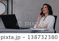 woman calling, office woman, modern desk. Cheerful career woman in formal white clothing speaks on her smartphone at her desk, surrounded by documents and her laptop. 138732380
