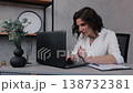 business concept, desk notes, career workspace. Professional woman in white outfit works intently on her laptop, focusing at her desk with papers and pen beside her. 138732381