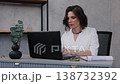business woman, focused woman, executive desk. Professional woman in white outfit focused on paperwork at her desk, with laptop and smartphone in stylish office setting. 138732392