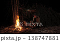 Man drinking hot beverage by campfire at night in winter forest shelter 138747881