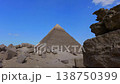 Pyramid of Khafre framed between large granite boulders with desert plateau and camels at Giza, Egypt. Unique perspective of ancient wonder under vivid blue sky. 138750399