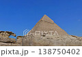 Pyramid of Khafre framed between large granite boulders with desert plateau and camels at Giza, Egypt. Unique perspective of ancient wonder under vivid blue sky. 138750402