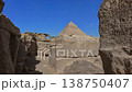 Pyramid of Khafre framed between large granite boulders with desert plateau and camels at Giza, Egypt. Unique perspective of ancient wonder under vivid blue sky. 138750407