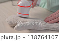A woman revives the look of her knitted garments with a lint remover. 138764107