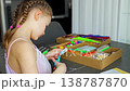 Little girl cutting paper with scissors while making craft at table with colorful materials. Kids creativity fine motor skills development and learning activity concept. 138787870