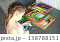 Little girl cutting paper with scissors while making craft at table with colorful materials. Kids creativity fine motor skills development and learning activity concept. 138788151