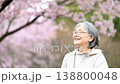 一位老婦人在櫻花樹下，櫻花飄落，臉上洋溢著笑容──這是春日裡健康快樂的象徵。慢動作捕捉老婦人仰望櫻花的畫面。 138800048