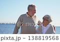 Senior mature couple smiling talking enjoying outdoor recreation walking on beach. Old husband wife on outdoor motion activity. Grandmother grandfather together enjoying walk. Family moment of love 138819568