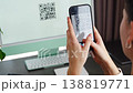 Person scanning QR code from computer screen with smartphone at home workspace. Digital interaction between devices and online service access concept. 138819771