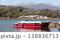 Small red boat Montenegro bay. Vessel floats on still water near rocky shore. High mountain range peaks appear in background under clear sky during daytime. Static shot captures peaceful scene. 138836713