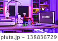 A 3D printer is actively creating a small object on a desk with spools of filament and a laptop displaying the word HOME 138836729