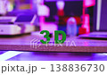 Green 3D letters stand on a wooden surface with a blurred background of a 3D printer and neon lights 138836730