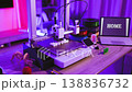 A 3D printer is actively creating the word HOME in white plastic filament on its build plate, with spools of filament and a laptop displaying the word HOME in the background 138836732