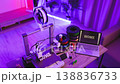 A 3D printer is actively creating the word HOME in white plastic filament, surrounded by spools of filament and a laptop displaying the word HOME 138836733