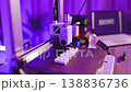A close-up view of a compact 3D printer in operation, illuminated by purple ambient light, with a laptop displaying the word HOME in the background 138836736