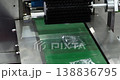 Small plastic sachets pass along conveyor under cleaning brush in packaging machine. Automated production stage with industrial equipment used in modern manufacturing process. 138836795