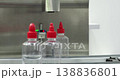 Clear plastic bottles with red caps pass through automated filling system for sauce production. Industrial packaging line with sensor control and modern machinery in food manufacturing. 138836801