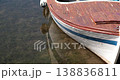 Wooden boat hull floating shore. Weathered vessel rests over shallow sea floor during sunny day. Aquatic grass stays visible through transparent waves. Bright light illuminates peeling wood 138836811