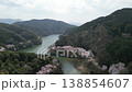 Aerial footage of cherry blossom trees in full bloom and mountain cherry trees in a park with a stream flowing through the mountains, filmed by a drone moving forward and ascending above. 138854607