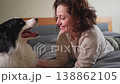Smiling woman playing with cute puppy dog border collie on bed at home indoor. Owner girl stroking holding dog friend sitting on sofa in living room. Love for pets friendship support team concept 138862105