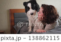 Smiling woman playing with cute puppy dog border collie on bed at home indoor. Owner girl stroking holding dog friend sitting on sofa in living room. Love for pets friendship support team concept 138862115