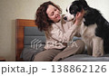 Smiling woman playing with cute puppy dog border collie on bed at home indoor. Owner girl stroking holding dog friend sitting on sofa in living room. Love for pets friendship support team concept 138862126