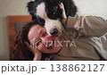 Smiling woman playing with cute puppy dog border collie on bed at home indoor. Owner girl stroking holding dog friend sitting on sofa in living room. Love for pets friendship support team concept 138862127