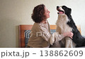 Smiling woman playing with cute puppy dog border collie on bed at home indoor. Owner girl stroking holding dog friend sitting on sofa in living room. Love for pets friendship support team concept 138862609