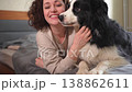 Smiling woman playing with cute puppy dog border collie on bed at home indoor. Owner girl stroking holding dog friend sitting on sofa in living room. Love for pets friendship support team concept 138862611