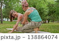 Group of women making a mermaid gentle yoga back stretch pose together in green summer park. Gentle yoga, stretch, park, group, women. 138864074