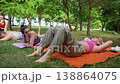 Women finishing yoga stretches relaxing on mats with children playing nearby in the grass. Finishing, yoga, stretching, relaxing, mats, children, grass. 138864075