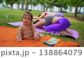 Mother and daughter practicing downward dog yoga pose together in orange mats in city park. Downward dog, yoga, mat, mother, daughter, city park. 138864079