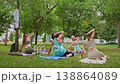 Group of women holding gentle yoga back stretch pose together in green summer park. Gentle yoga, stretch, park, group, women. 138864089