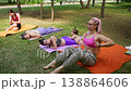 Yoga instructor assisting in exercises for the abs and deep core muscles on mats during group outdoor fitness class in park. Side stretch, assistance, mats, yoga, instructor, fitness, park. 138864606