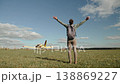 Caucasian man stands and throws arms up on sunny day in field near light aircraft on back view. Traveler joy and freedom of air travel. 138869227