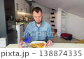 Caucasian Man Grimacing After Spicy Bite, Sipping Water From Glass Between Forks Of Potato And Pepper, Denim 138874335