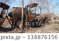 Row Of Rusted Harvesters Between Birch, Thin Trunks And Dried Leaves Weaving Through Corroded Metal, Cracked Cabins And Exposed Combs, Spring Sunlight And Undergrowth, Nature Reclaiming 138876156