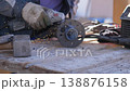 Closeup Hands Grinding Metal Flange, Sparks Scatter Across Wooden Bench As Technician Uses Angle Grinder With Protective Gloves To Clean Flange Surface, Tool Cords And Rough Workshop 138876158