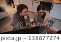 Two women look at laptop while sitting at table in modern kitchen space 138877274